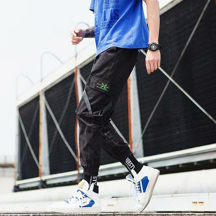 Man wearing black hip hop jogger pants with green graphics, paired with blue shirt and stylish sneakers. Perfect for casual streetwear.