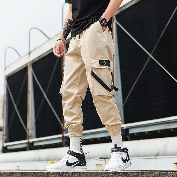 Model wearing beige hip hop jogger pants with pockets, styled with white sneakers and a black shirt.